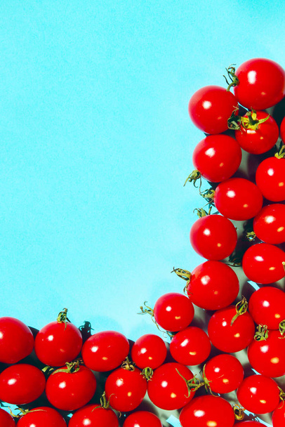 青い背景に赤いチェリートマト、垂直方向のイメージ。カラフルな食品の背景。広告、メニュー、食材のコンセプト. - 写真・画像