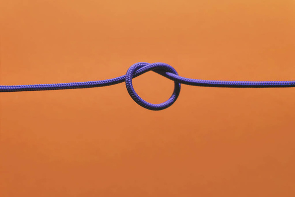knot of braided wire of lilac color on an orange background - Zdjęcie, obraz