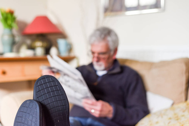 Зрелый пенсионер, сидящий на диване и читающий новости.
 - Фото, изображение