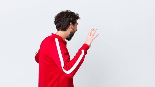 young bearded man back view screaming in panic or anger, shocked, terrified or furious, with hands next to head against copy space wall - Fotoğraf, Görsel