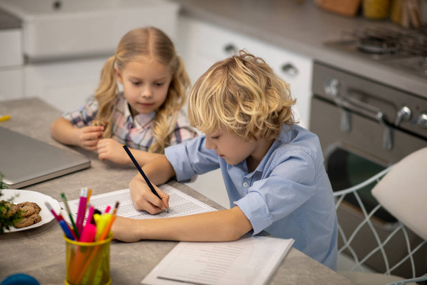 Two kids sitting at the table and looking busy with drawing - Photo, image