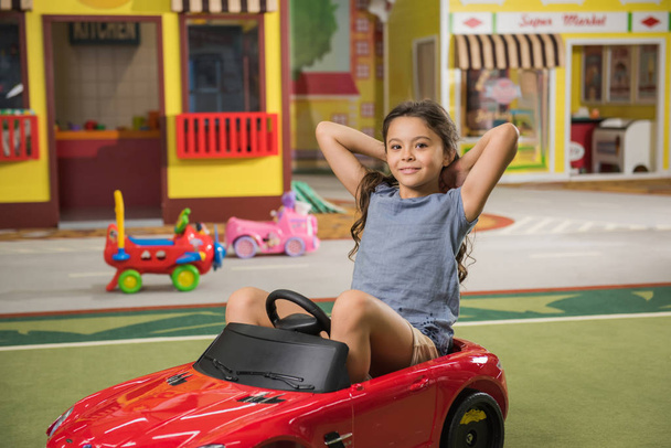 Happy little girl sitting in toy car at indoor playground. - Photo, Image
