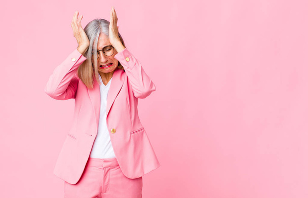 middle age cool woman feeling stressed and anxious, depressed and frustrated with a headache, raising both hands to head against flat wall - Foto, Imagen