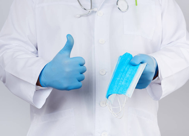 médico con una capa blanca, guantes estériles de látex azul sostiene textil
  - Foto, Imagen