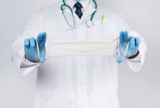 médico con una capa blanca, guantes estériles de látex azul sostiene textil
  - Foto, Imagen