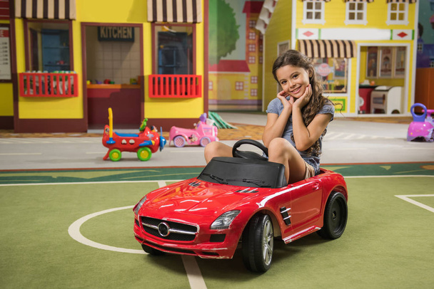 Όμορφο κοριτσάκι με μίνι αυτοκίνητο στο κέντρο του παιχνιδιού. - Φωτογραφία, εικόνα