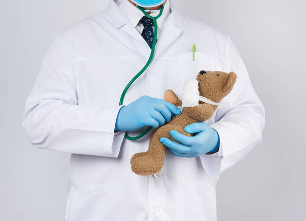 pediatrician in a white coat, blue latex gloves holds a brown te - Photo, Image