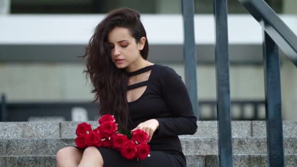 Kobieta z bliska siedząca z różami. Kobieta dotykając bukiet róż na schodach - Materiał filmowy, wideo
