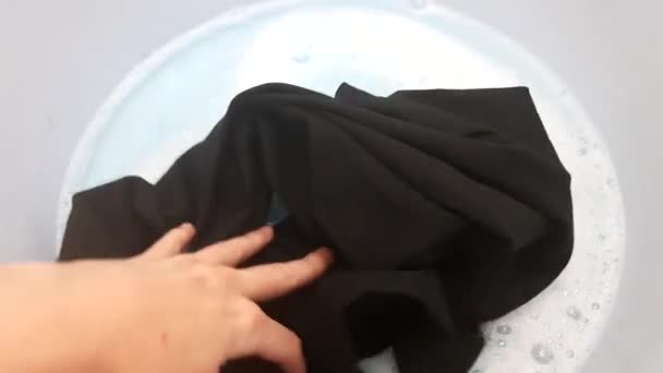 Eine weibliche Hand legt ein schmutziges Ding in ein blaues Becken mit Wasser und weißen Blasen. Schmutzwäsche mit Waschmittel waschen - Filmmaterial, Video