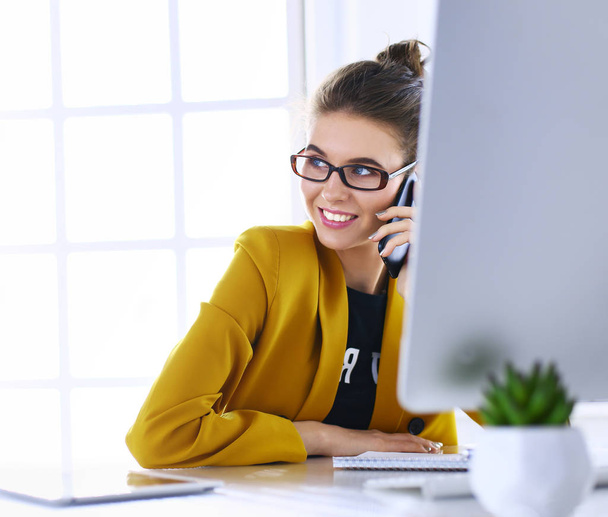 Businesswoman sitting in office with laptop on telephone - Zdjęcie, obraz