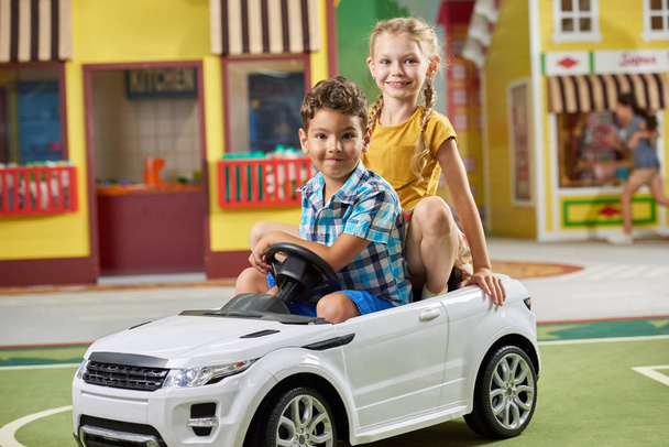 Twee kinderen zitten in een speelgoedauto en kijken naar de camera. - Foto, afbeelding
