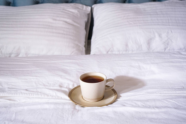 Чашка чая на белой кровати, крупным планом. Утренняя концепция Оформление и мебель в современной спальне
. - Фото, изображение