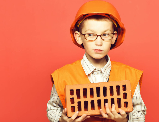 young cute builder boy on red studio background, copy space - Foto, Bild