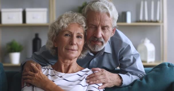 Loving elderly husband embracing sitting on couch smiling hoary woman. - Video, Çekim