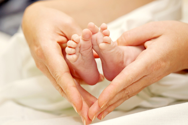 τα χέρια της μητέρας με τα πόδια από το νεογέννητο μωρό. - Φωτογραφία, εικόνα