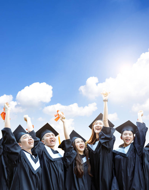 estudantes felizes em vestidos de graduação titulares de diplomas sobre fundo nuvem
 - Foto, Imagem