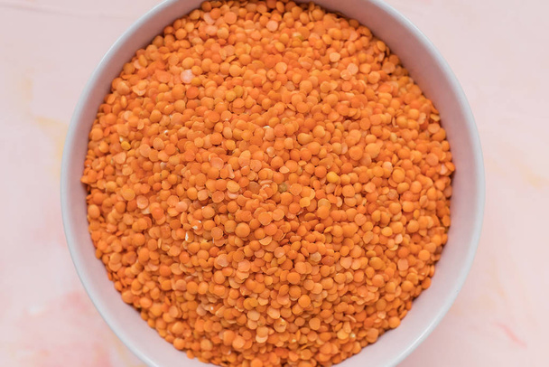 Red lentils in ceramic bowl on pink background - Photo, Image