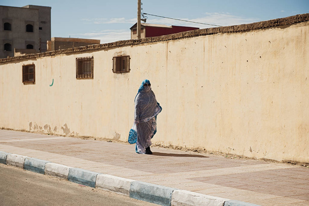 Nők sétálnak az utcán, gyönyörű kék-fehér arab ruhákban. Épületek háttere. - Fotó, kép