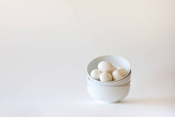 Stack di ciotole bianche con uova bianche su sfondo bianco
 - Foto, immagini