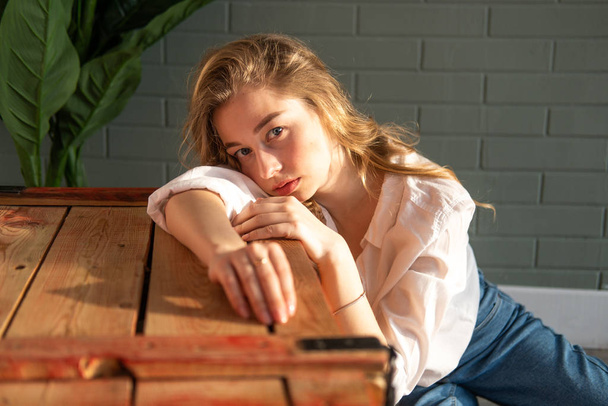 Young beautiful woman sitting on the floor next to wooden box and green plant - Foto, immagini