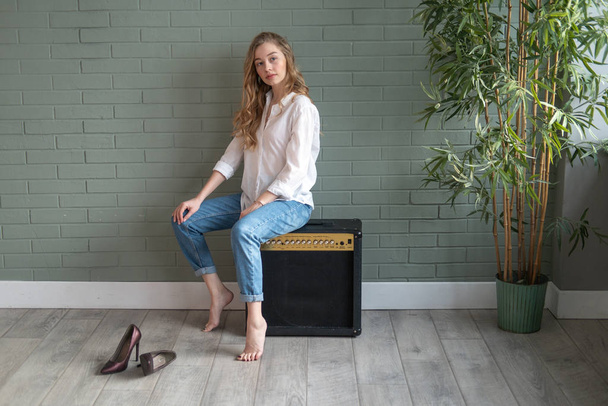 Young beautiful woman sitting on subwoofer with bare feet next to green plant - 写真・画像