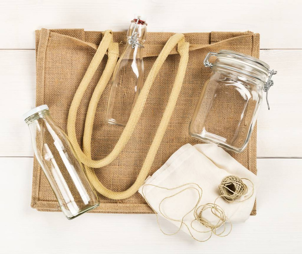 Zero waste or waste free shopping utensils with burlap bag, glass bottles and cotton bag on white wooden table background flat lay from above - Valokuva, kuva