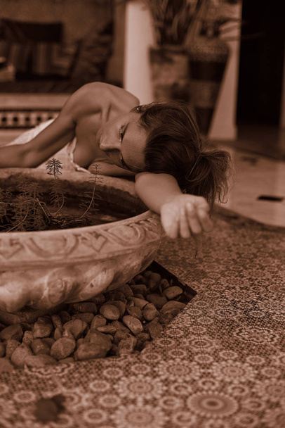 Attraktives weibliches Model in bauchfreiem Top, elegantem, authentischem Rock, posiert auf dem Boden in hellem, geöffnetem arabischen Raum und genießt Freiheit, Jugend und Selbstvertrauen. Sepiafarben. Schönheit, Modekonzept. - Foto, Bild