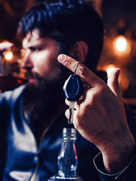 Man with beard holds glass brandy. Macho drinking. Confident man with car keys in his hand. Do not drink and drive Cropped image of drunk man talking car keys. - Photo, Image