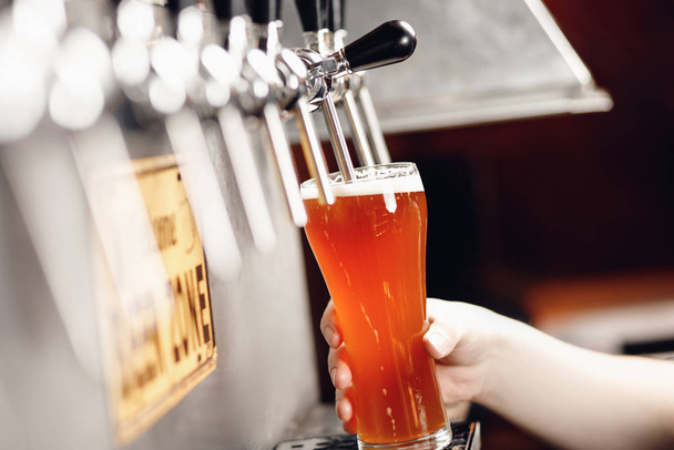 Джет свіжого легкого пива наливається в скляну чашку на темному тлі з бризками та піною
 - Фото, зображення