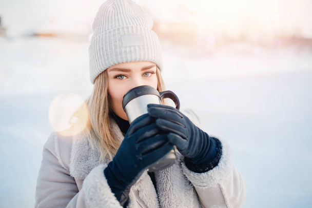 Mujer sosteniendo la copa de invierno fondo borroso claro. Chica manos con café caliente, té o cacao. Concepto vacaciones de Navidad
 - Foto, imagen