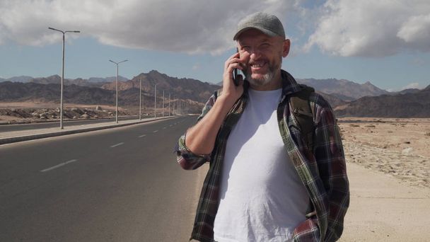 όμορφος ανώτερος άνδρας μιλάει από smatrphone στέκεται σε ένα δρόμο στην έρημο - Φωτογραφία, εικόνα