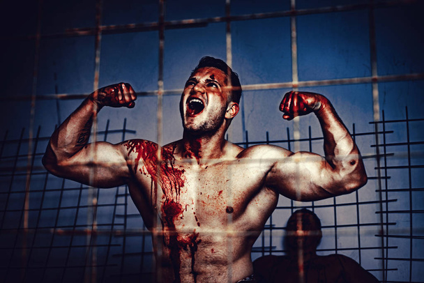Scary monster just murdered his victim. Strong aggressive monster behind grid. Prison for monster. Psycho mad man. Murderer mythical creature. Muscular man soiled with red blood. Halloween concept - Photo, image