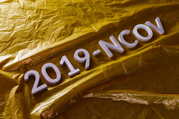 Het woord 2019-Ncov gelegd met metalen letters op gele verfrommelde plastic film achtergrond in schuine diagonale samenstelling - Foto, afbeelding
