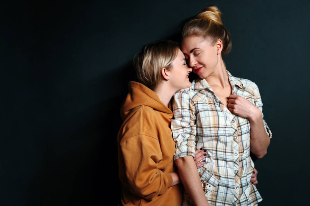 Portrait of young gay couple, lesbian women hugging on black background with copy space. Concept of love, family, gay marriage and pride - 写真・画像