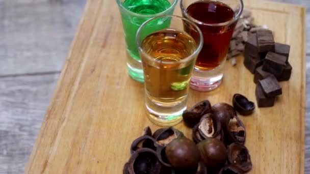 Three shots with different colors of alcoholic beverages and ingredients for their preparation rotate on a wooden kitchen Board - Footage, Video