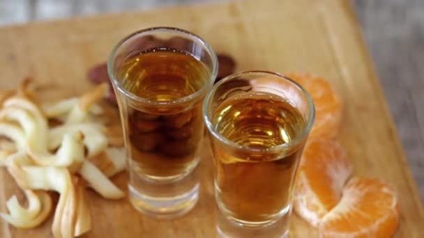 Twee shots met zelfgemaakte whisky, verschillende hapjes en jam van kegels en veenbessen draaien op een houten statief - Video