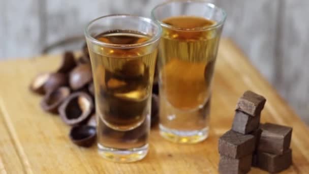 Twee shots met zelfgemaakte whisky en ingrediënten voor hun bereiding draaien op een houten statief - Video