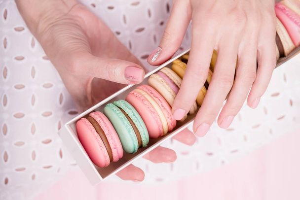Beautiful female hands holding gift box of delicious french colorful macaroons on pink background. Top view, copy space - Photo, Image