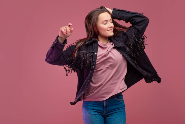 cheerful girl in a fringed jacket dances on a pink background. - Photo, image