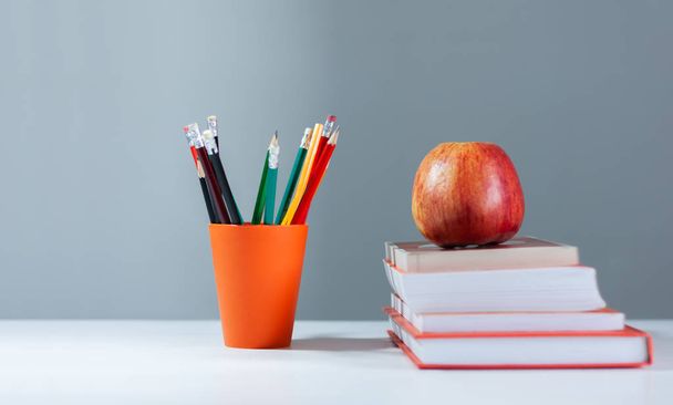 Orange pencil holder, stack of books on white table with red app - Photo, Image