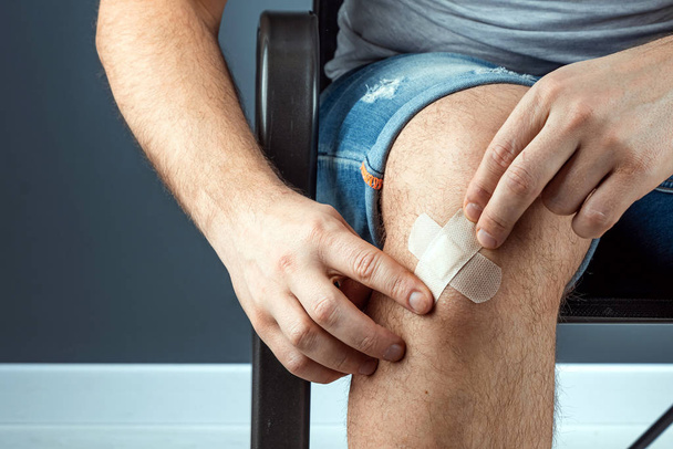 A man seals a wound on his knee with adhesive plaster close-up. Ambulance, body care, knee injuries. - Zdjęcie, obraz