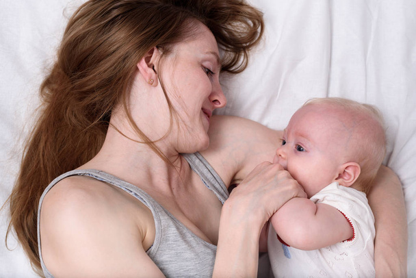 Мама с новорожденным лежала на белом одеяле. Любящая мать обнимает своего ребенка
 - Фото, изображение