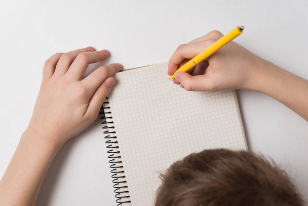 Child writes in notebook. Doing homework. White background. Top view - Foto, imagen