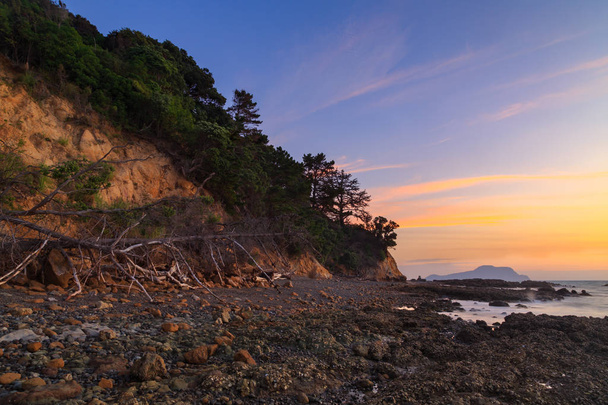 Захід сонця над кам'яним пляжем і прибережними скелями на півострові Коромандел (Нова Зеландія). - Фото, зображення