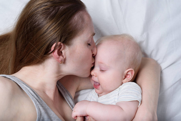 Mãe feliz segurando criança infantil a mãos. Bela jovem mãe beijando seu bebê
. - Foto, Imagem