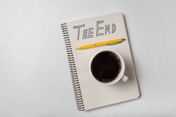 Copybook met The End tekst. Kladblok, pen en kopje koffie op witte achtergrond - Foto, afbeelding