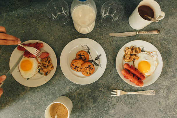 Breakfast set of sausages fried eggs and mushroom with fresh milk and cookies served on the table. - 写真・画像
