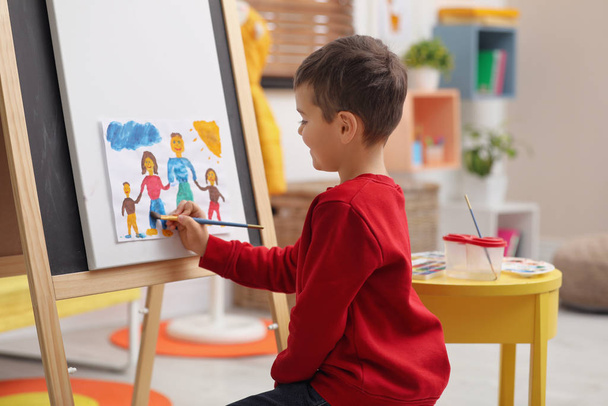Little child painting on easel in room - Φωτογραφία, εικόνα