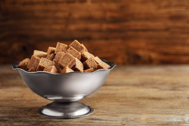 Brown sugar cubes in metal bowl on wooden table. Space for text - Foto, Imagen