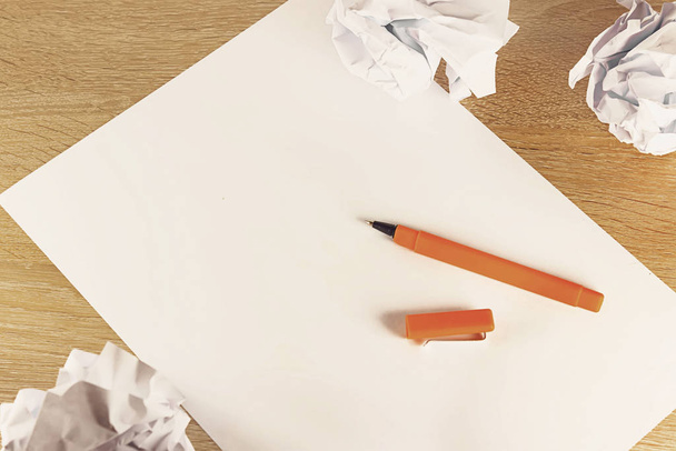A blank sheet of paper and a pen on a light wooden table with crumpled paper balls . A ballpoint pen lying on a piece of paper, copy space - Photo, Image